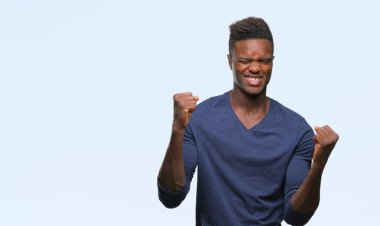 Gülümseyen ve başarı için çığlık genç Afro-Amerikan adam izole arka plan çok mutlu ve heyecanlı kaldırdı, silah ile kazanan jest yapıyor. Kutlama kavramı.