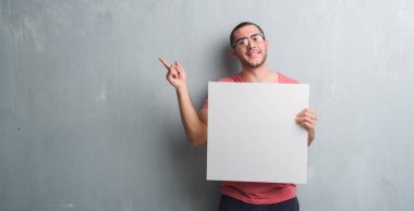 Boş bir afiş çok mutlu el ve parmak ile tarafına işaret tutan gri grunge duvarın üzerinden beyaz delikanlı