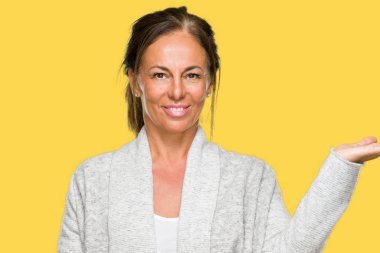 Neşeli sunulması ve kameraya bakarak avucunun ile işaret gülümseyen izole arka plan üzerinde kış kazak giyen güzel orta yaş yetişkin kadın.