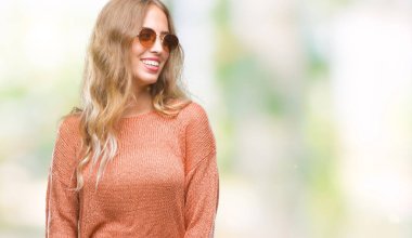 Güzel genç sarışın kadın uzak tarafına yüzünde, doğal ifade gülümseme ile seyir izole arka plan üzerinde güneş gözlüğü takıyor. Kendine güvenen gülüyor.