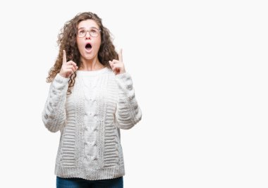 İzole arka plan üzerinde kış kazak giyen genç kız hayran ve yukarıya bakıp parmakları ile işaret şaşırttı ve silah kaldırdı güzel esmer kıvırcık saç.