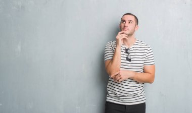 Beyaz delikanlı çene düşünme hakkında soru, dalgın ifade üzerine el ile gri grunge duvarın üzerinden. Düşünceli yüzüyle gülümsüyor. Şüphe kavramı.