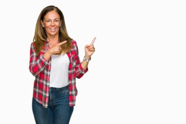 Orta yaş yetişkin kadın gülümseyerek ve iki elleri ve parmakları ile tarafına işaret kamera bakarak izole arka plan üzerinde rahat gömlek giymiş.
