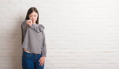 Genç Çinli kadın kamera ve size parmak ile işaret tuğla duvarın üzerinden el işareti, pozitif ve kendinden emin bir jest ön