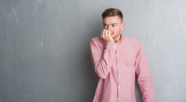 Genç Kızıl saçlı adam stresli ve gergin elle çivi ısırma ağzına bakarak pembe gömlek giymiş gri grunge duvarın üzerinden. Anksiyete sorunu.