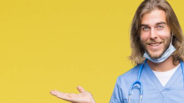 Neşeli sunulması ve kameraya bakarak avucunun ile işaret gülümseyen izole arka plan üzerinde uzun saçlı Genç yakışıklı Doktor adam.