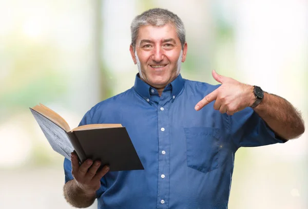 英俊的高级教师在孤立的背景下阅读一本书 惊讶地把手指指向自己 — 图库照片