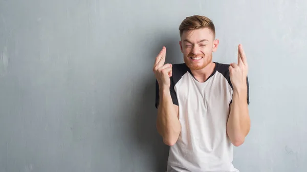 Joven Pelirrojo Sobre Pared Gris Grunge Sonriendo Cruzando Los Dedos —  Fotos de Stock