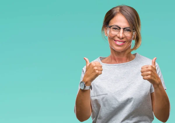 中年资深西班牙裔妇女戴眼镜在孤立的背景下成功的标志做积极的手势与手 大拇指向上微笑和快乐 看着带着欢快表情的相机 胜利者的手势 — 图库照片