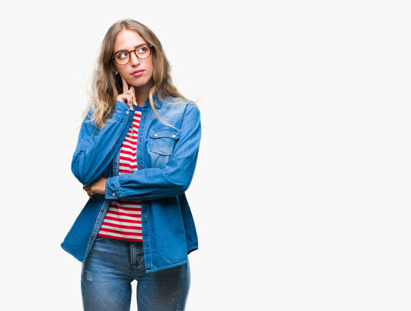 Beautiful young blonde woman wearing glasses over isolated background with hand on chin thinking about question, pensive expression. Smiling with thoughtful face. Doubt concept.