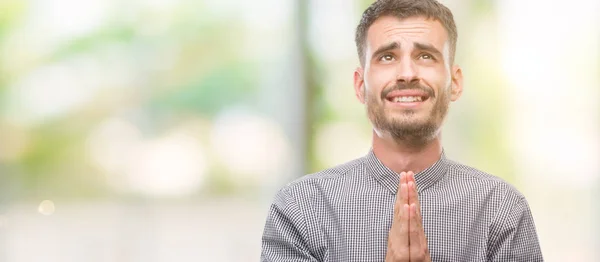 Young hipster man begging and praying with hands together with hope expression on face very emotional and worried. Asking for forgiveness. Religion concept.