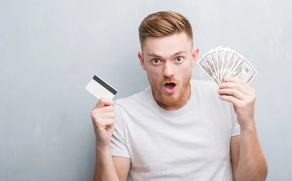 Young Redhead Man Holding Dollars Credit Card Scared Shock Surprise — Stock Photo, Image