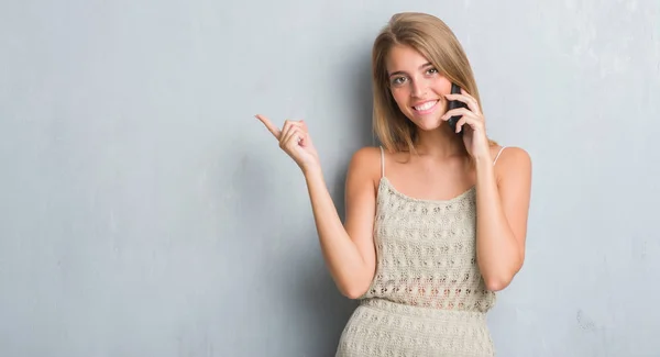 グランジ灰色の壁側の手と指で指す非常に幸せの電話で話して美しい若い女性 — ストック写真