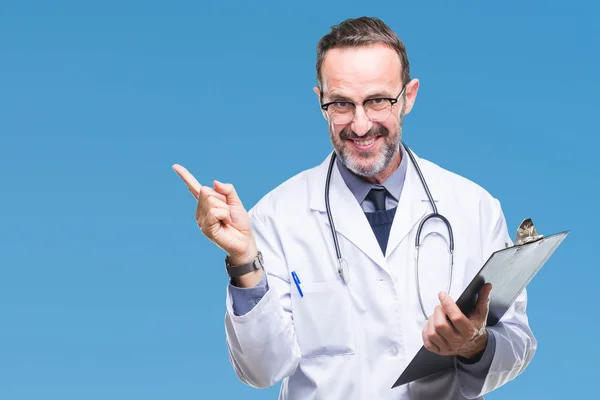 中年资深医生人拿着剪贴板在孤立的背景非常高兴地指着手和手指的侧面 — 图库照片