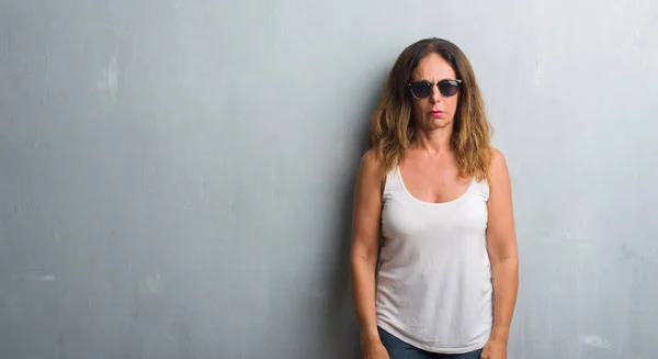 身に着けているサングラス懐疑論者と神経 しかめっ面の動揺問題のため灰色の壁を越えて中年のヒスパニック系女性 否定的な人 — ストック写真