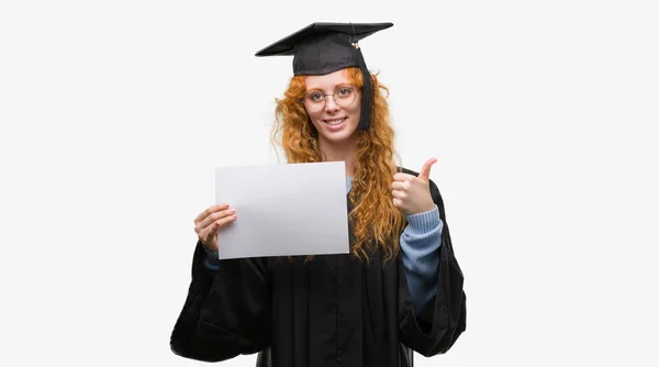 年轻的红发女郎穿毕业制服持有度快乐与大微笑做 拇指与手指 优秀的标志 — 图库照片