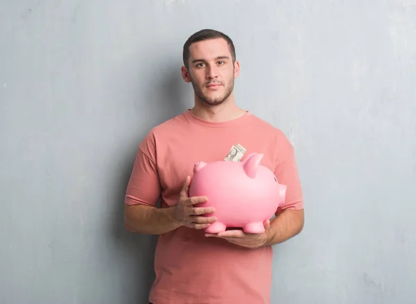 Young Caucasian Man Grey Grunge Wall Holding Piggy Bank Confident — Stock Photo, Image