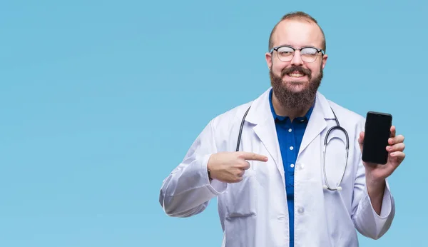 Young doctor man showing smartphone screen over isolated background with surprise face pointing finger to himself