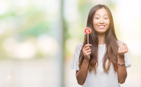 孤立した背景に棒付きキャンディーを食べる若いアジア女性 — ストック写真