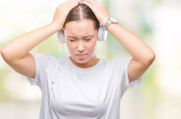 年轻的白种女人听音乐戴着耳机在孤立的背景下头痛绝望和紧张 因为疼痛和偏头痛 手在头上 — 图库照片
