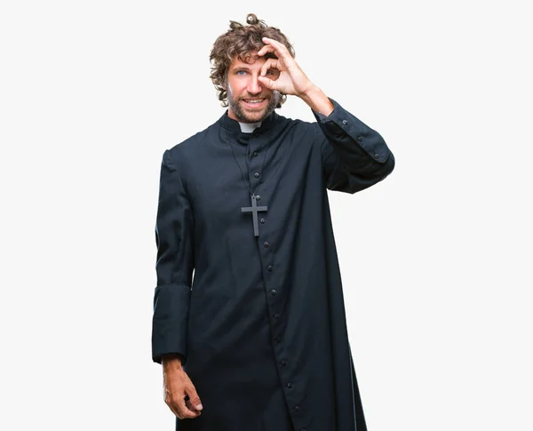 英俊的天主教牧师在孤立的背景做确定的手势与手微笑 眼睛通过手指看与愉快的面孔 — 图库照片