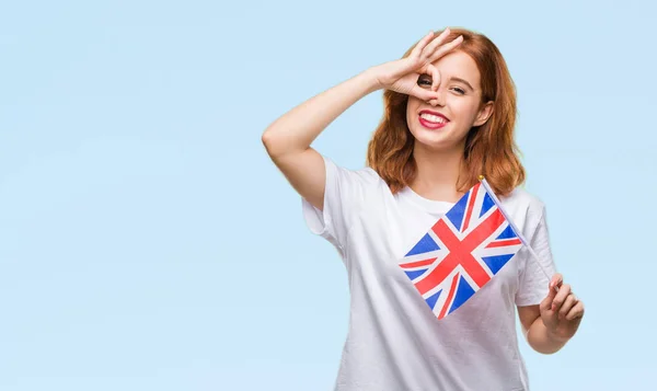 孤立した背景に指を通して見る目に手で サインをして笑っている幸せそうな顔でイギリスの旗を保持している若い美しい女性 — ストック写真