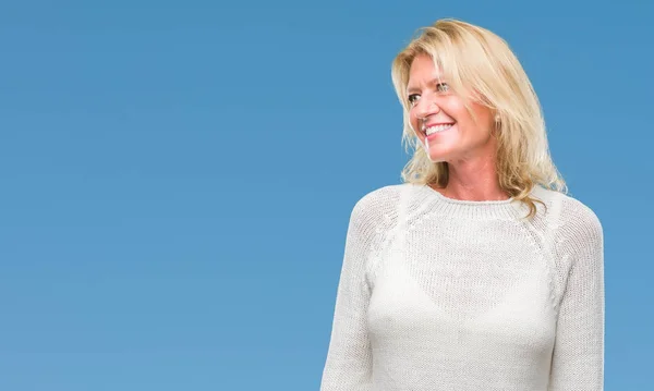 Middle age blonde woman wearing winter sweater isolated background looking away to side with smile on face, natural expression. Laughing confident.