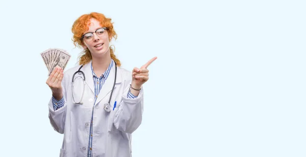 Joven Doctora Pelirroja Sosteniendo Dólares Muy Feliz Apuntando Con Mano — Foto de Stock