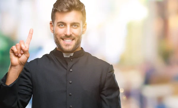 年轻的天主教基督教牧师男子在孤立的背景显示和指向的手指头号 而微笑着自信和快乐 — 图库照片