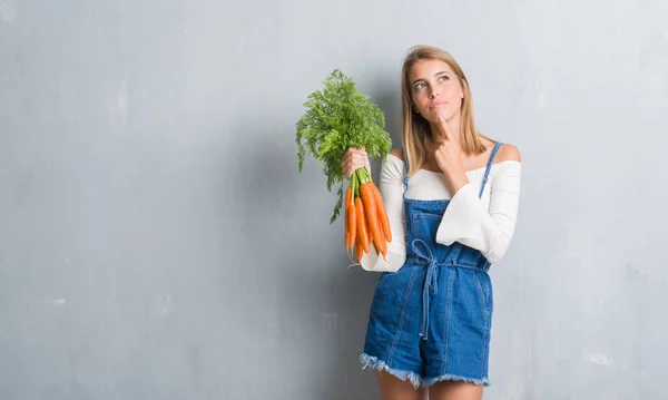 Vacker Ung Kvinna Över Grunge Grå Väggen Håller Färska Morötter — Stockfoto