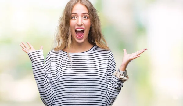 stock image Beautiful young blonde woman wearing stripes sweater over isolated background celebrating crazy and amazed for success with arms raised and open eyes screaming excited. Winner concept