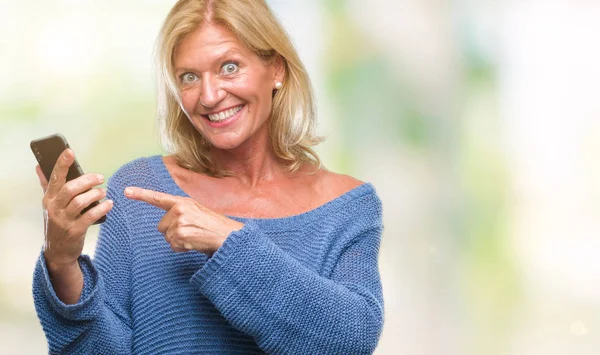 Middle age blonde woman sending message using smartphone over isolated background very happy pointing with hand and finger