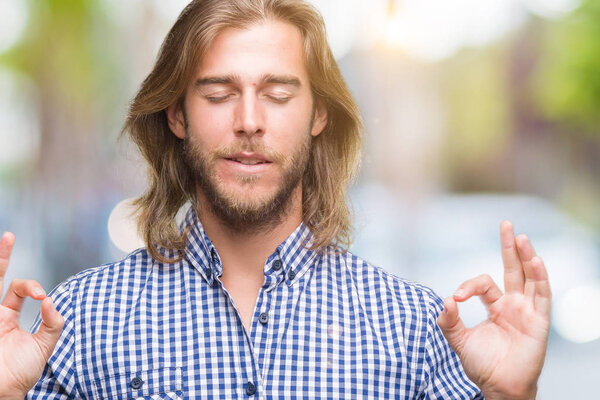 Young handsome man with long hair over isolated background relax and smiling with eyes closed doing meditation gesture with fingers. Yoga concept.