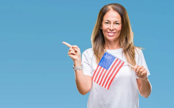 Middle age hispanic woman holding flag of United States of America over isolated background very happy pointing with hand and finger to the side
