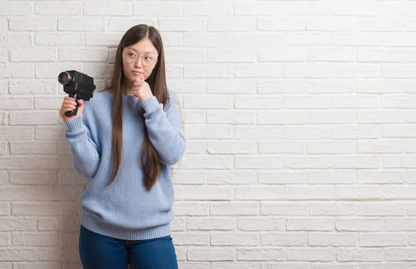 年轻的中国女子拍摄拿着摄像机严肃的脸思考问题 很困惑的想法 — 图库照片