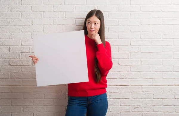 Young Chinese Woman Brick Wall Holding Banner Serious Face Thinking — Stock Photo, Image