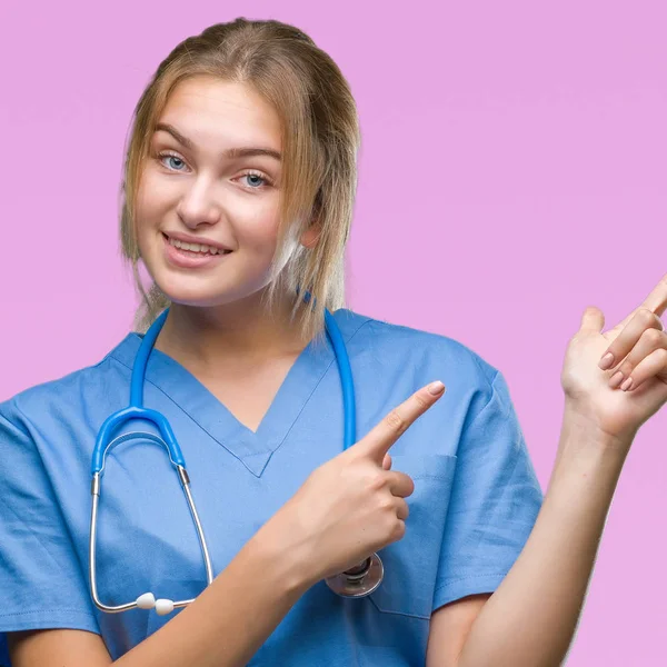 年轻的高加索医生妇女穿着外科医生制服在孤立的背景微笑着 看着相机指向镜头 用两只手和手指指向一边 — 图库照片