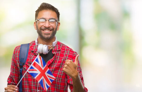 イギリスのパスポートを保持している大人のヒスパニック学生男笑顔の サイン 優秀な兆候を親指をやって幸せなバック グラウンドを分離しました — ストック写真