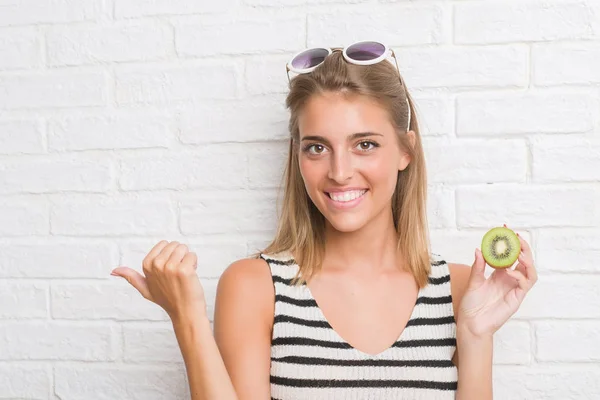 Beautiful Young Woman White Brick Wall Eating Green Kiwi Pointing — Stock Photo, Image