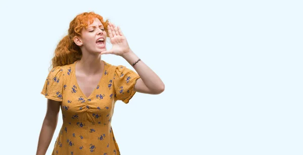 Young redhead woman shouting and screaming loud to side with hand on mouth. Communication concept.