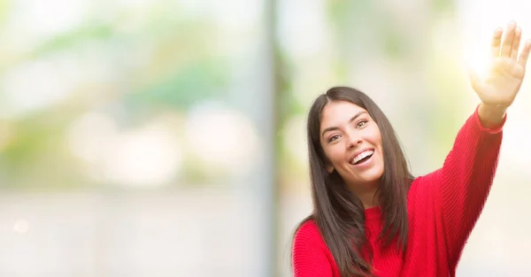 年轻美丽的西班牙裔穿着红色毛衣看着相机微笑着张开双臂拥抱 快乐的表达拥抱幸福 — 图库照片