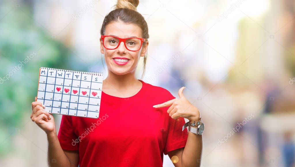 Young beautiful woman holding menstruation calendar over isolated background with surprise face pointing finger to himself