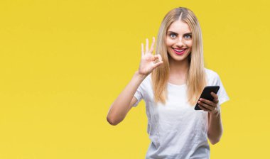 Genç güzel sarışın kadın parmakları, mükemmel sembolü olan ok işareti yapıyor izole arka plan üzerinde akıllı telefon kullanma
