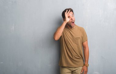 Sürpriz yüz, göz parmaklarının arasından seyir ile ok jest yapıyor gri grunge duvarın üzerinden yakışıklı genç adam şok. İmansız ifade.