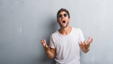 Çılgın ve kızgın bağırarak ve agresif ifade ve silah kaldırdı bağırmaya güneş gözlüğü takıyor gri grunge duvarın üzerinden yakışıklı genç adam. Hayal kırıklığı kavramı.