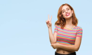 Genç güzel kadın mutlu yüz zafer işareti yaparken kameraya göz kırpıyor ile gülümseyen izole arka plan yüzünden. İki numaralı.