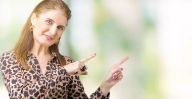 Gülümseyen ve iki elleri ve parmakları ile tarafına işaret kamera bakarak izole arka plan üzerinde leopar elbise giyen güzel orta yaş olgun zengin kadın.