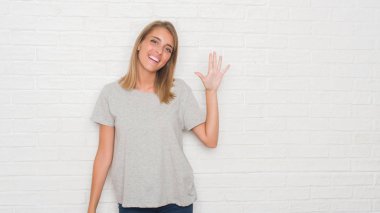 Güzel ve genç birbayan gösterilen ve parmakları ile işaret beyaz tuğla duvarın üzerinden beş kendinden emin ve mutlu gülümseyerek iken numara.