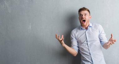 Genç redhead iş adamı gri grunge duvarın çılgın ve kızgın üzerinden bağırarak ve agresif ifade ve silah kaldırdı bağırıyordu. Hayal kırıklığı kavramı.