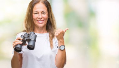 Orta yaş İspanyol kadın dürbün ile ok işareti, başparmak ile parmak, mükemmel işareti yapıyor kocaman bir gülümseme ile izole arka plan üzerinde mutlu arıyor